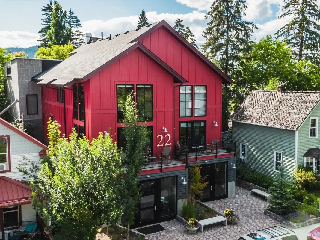 Un edificio rojo de varios niveles está junto a casas vecinas, con árboles y un patio pavimentado.