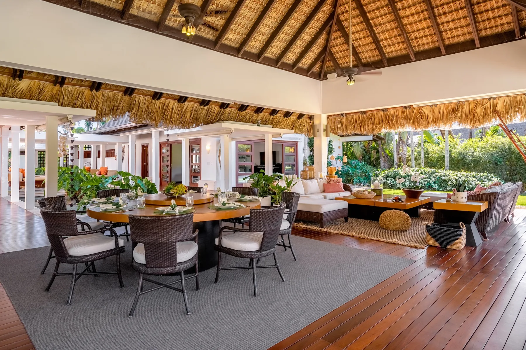 An open-air lounge and dining area with seating beneath a thatched roof.