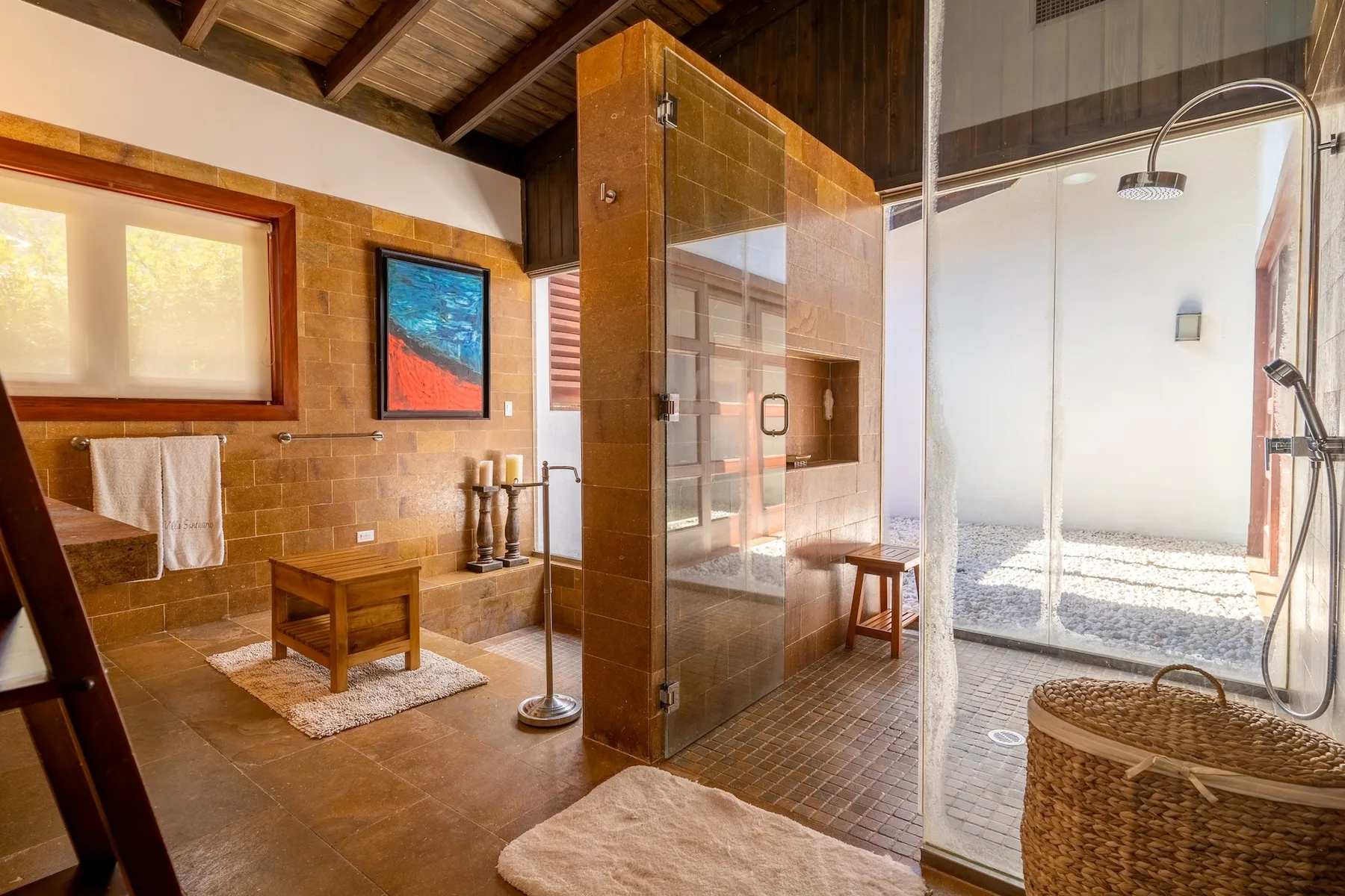A bathroom with a glass shower, wooden surfaces, and a small seating area.