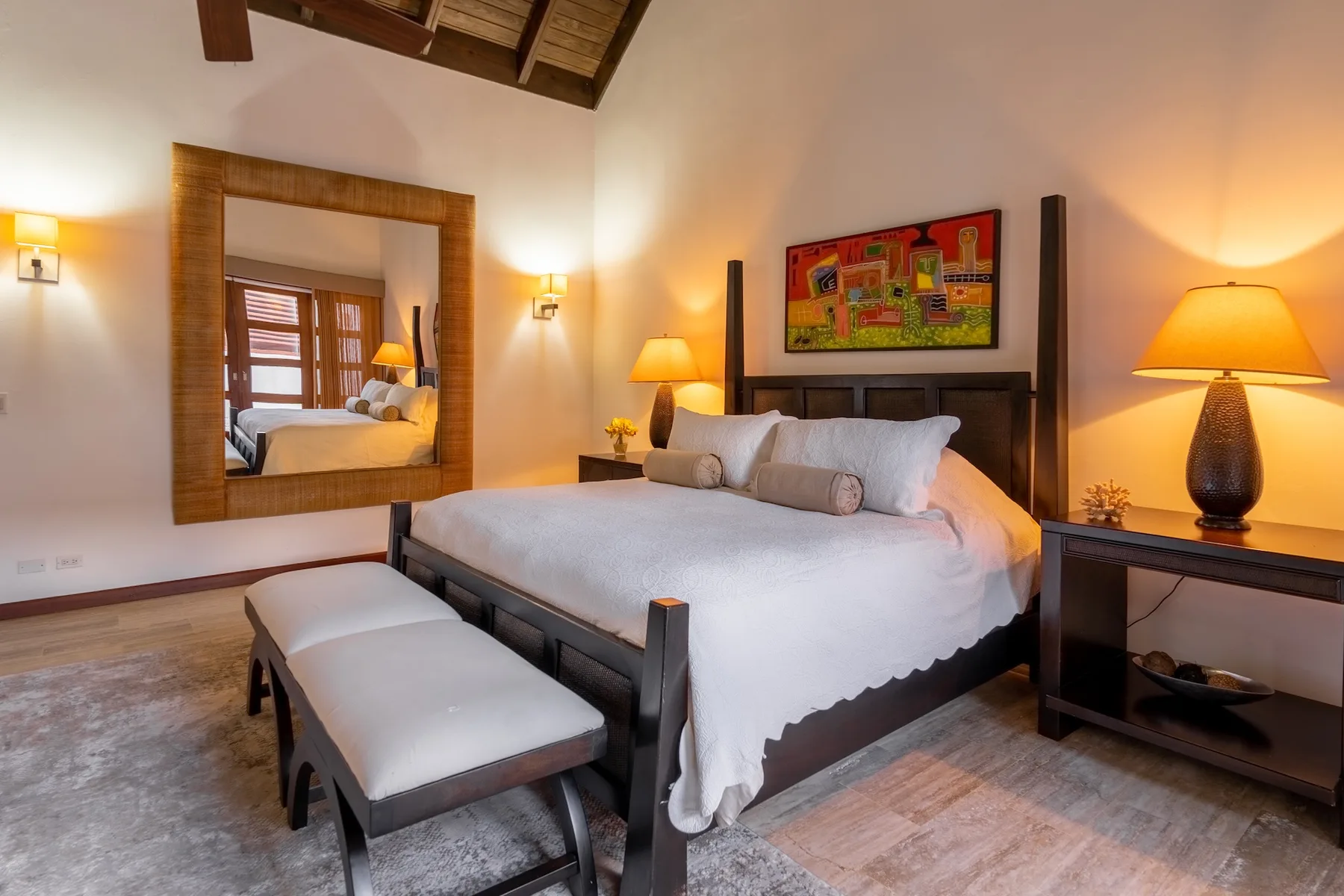 A bedroom with a large bed, cushioned bench, and colorful artwork above the headboard.