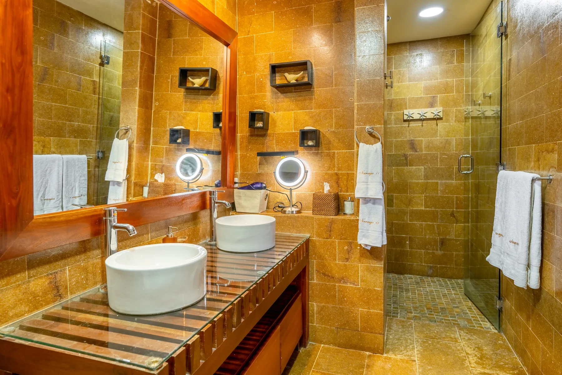 A tiled bathroom with a vanity, basin, and glass-enclosed shower.