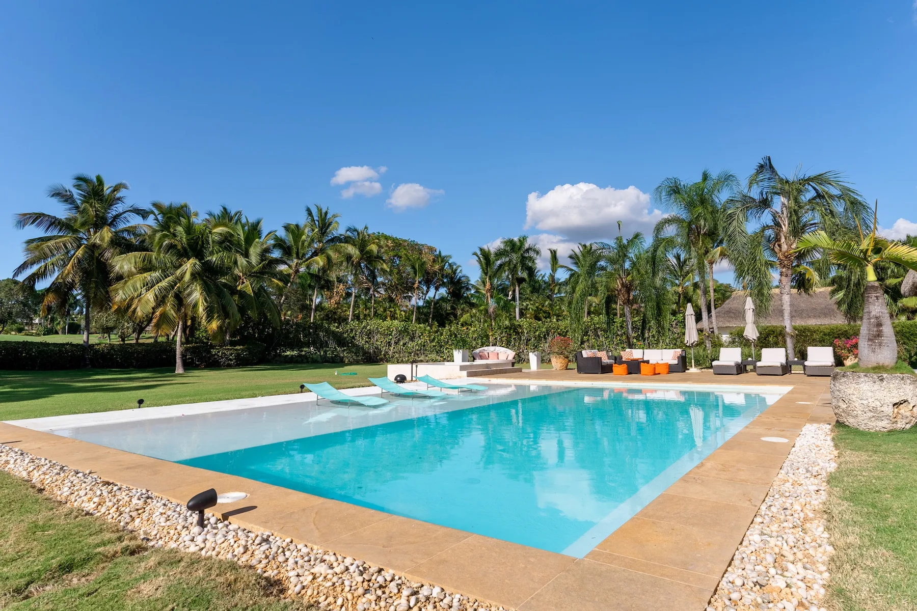 A swimming pool beside a landscaped lawn, palm trees, and outdoor seating.