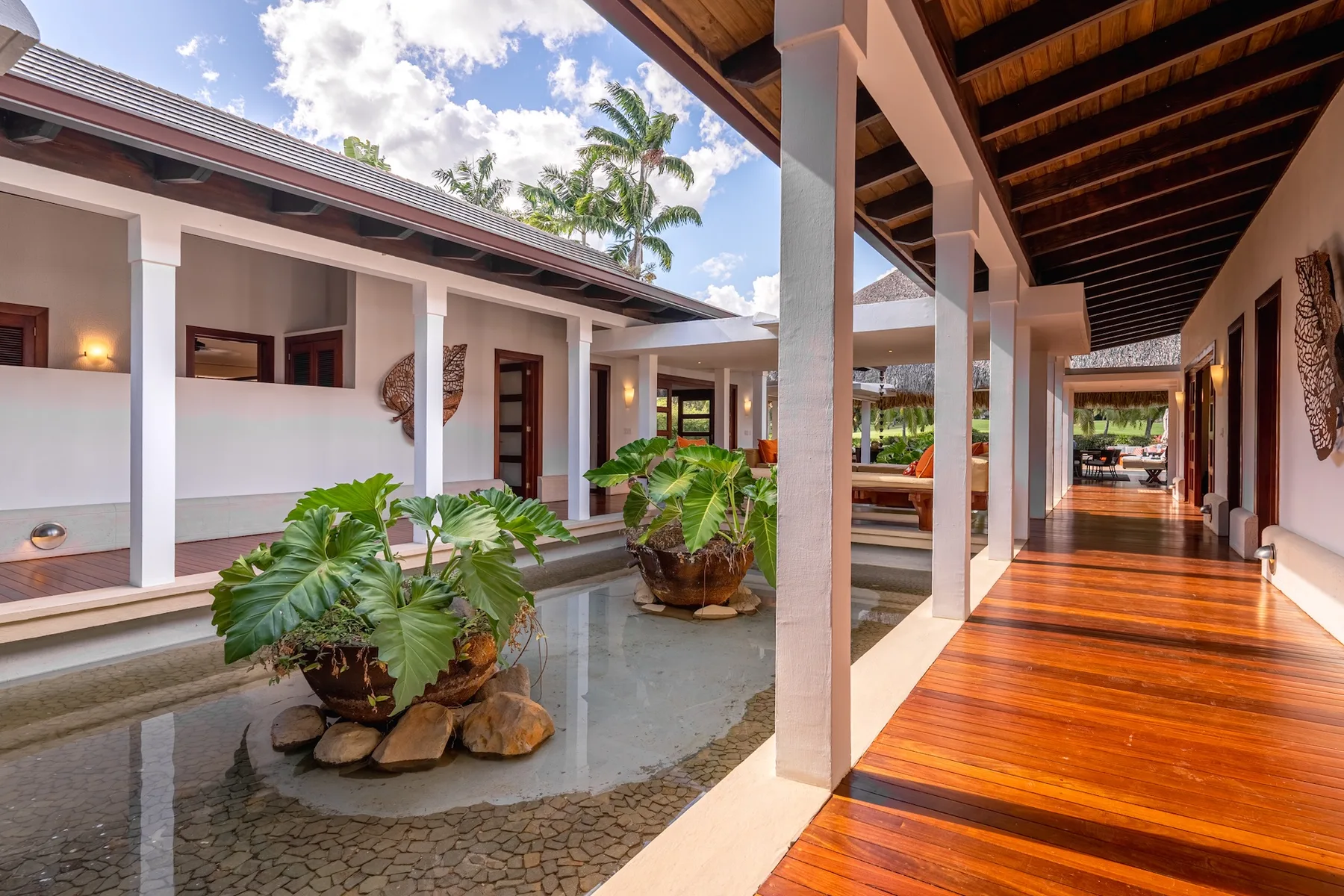 A covered wooden walkway beside a shallow water feature and potted plants.