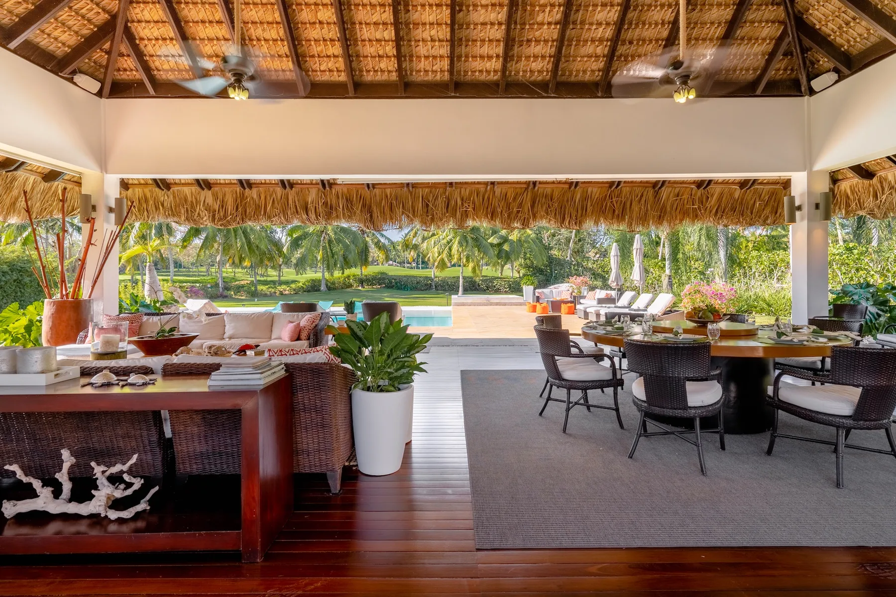 An open-air dining area with tables and seating overlooks a swimming pool and palm trees.