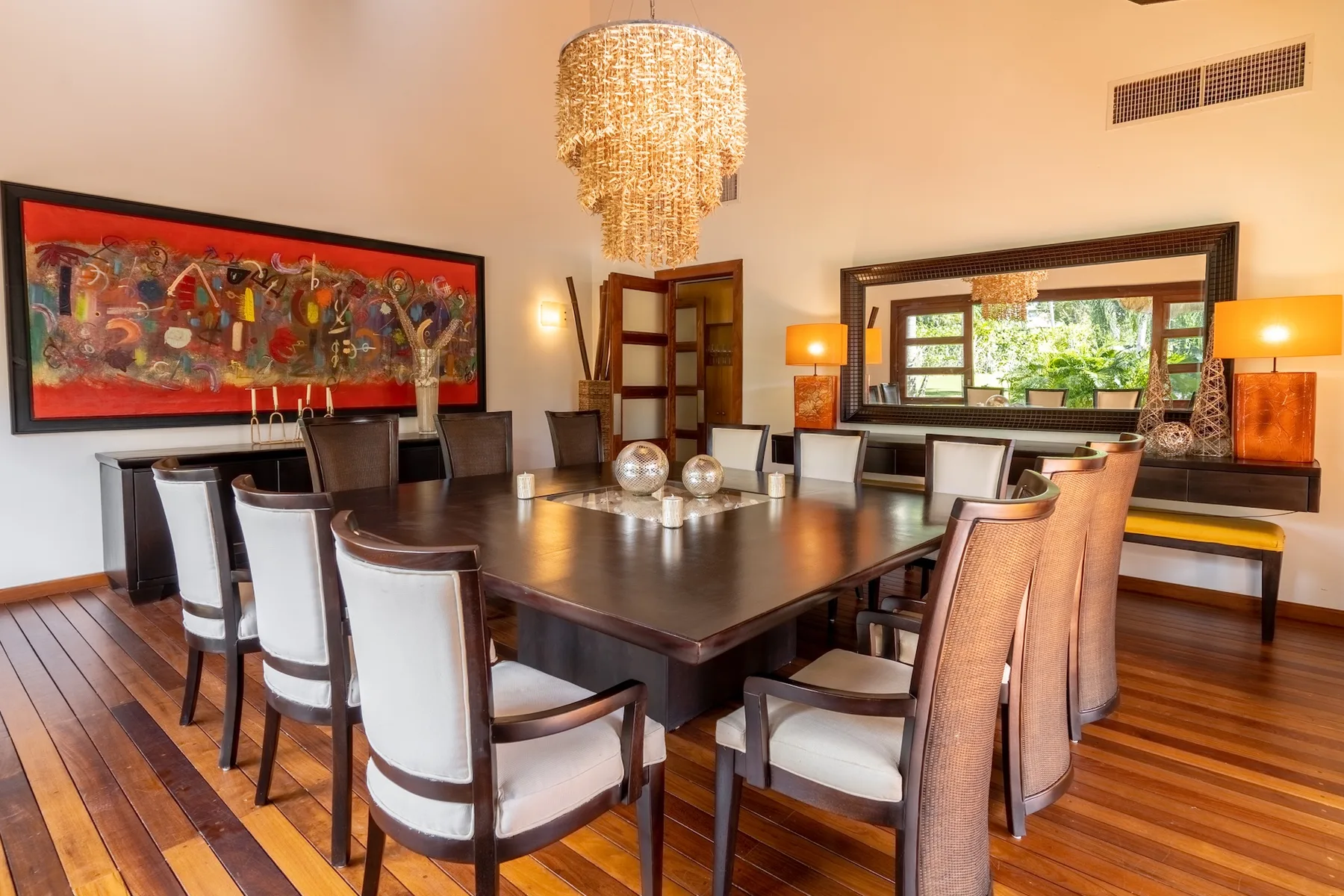 A dining room with a long table and upholstered seating beneath a chandelier.