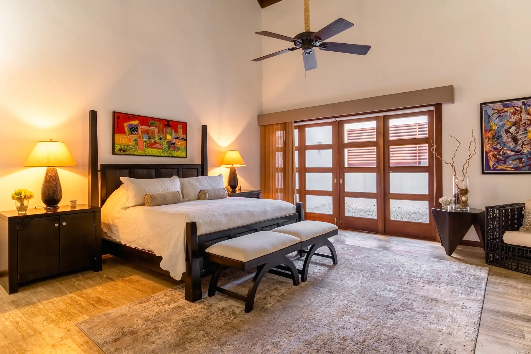 A bedroom with a large bed, bedside tables, and wide windows.