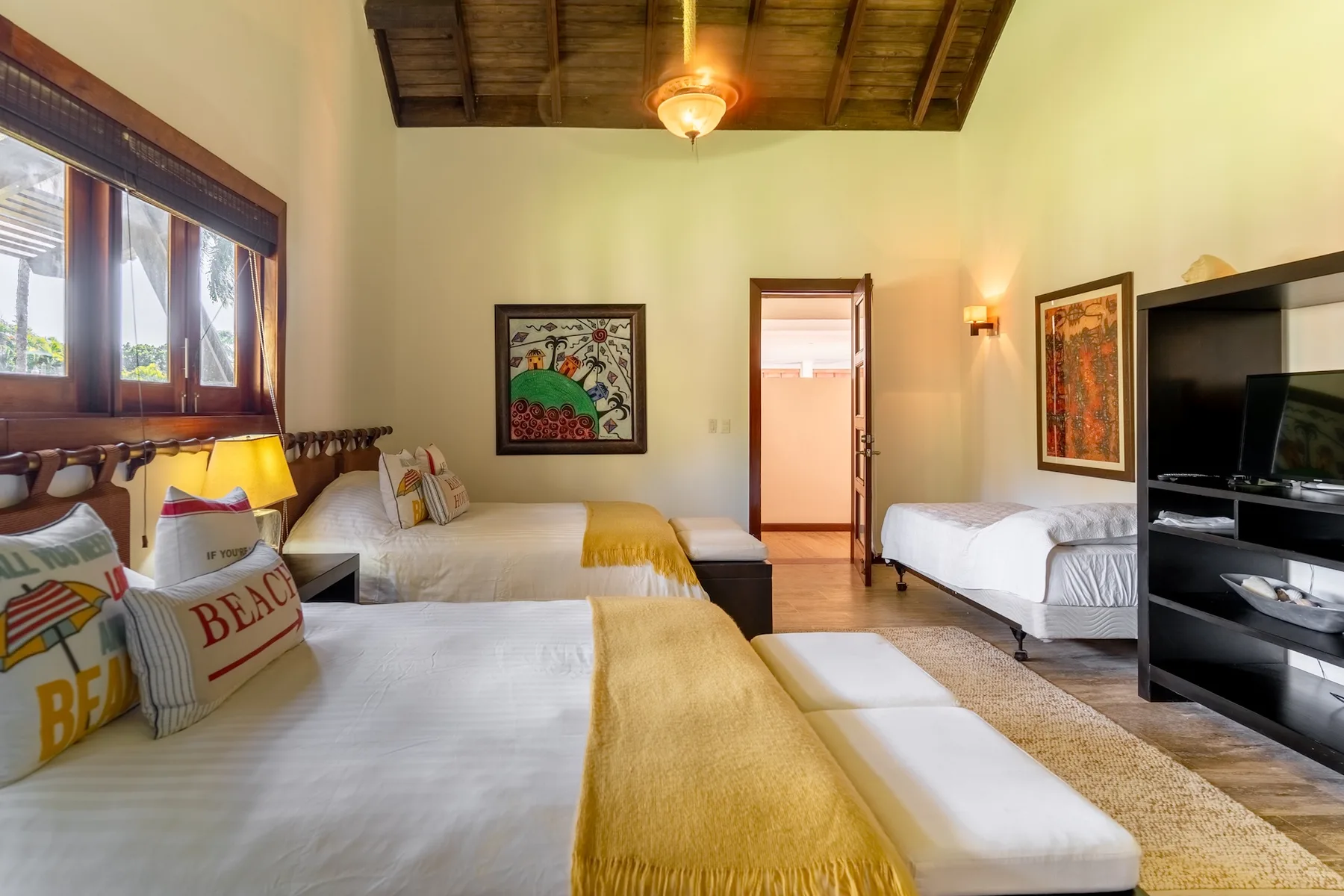 A bedroom with several beds, colorful wall art, and a television.