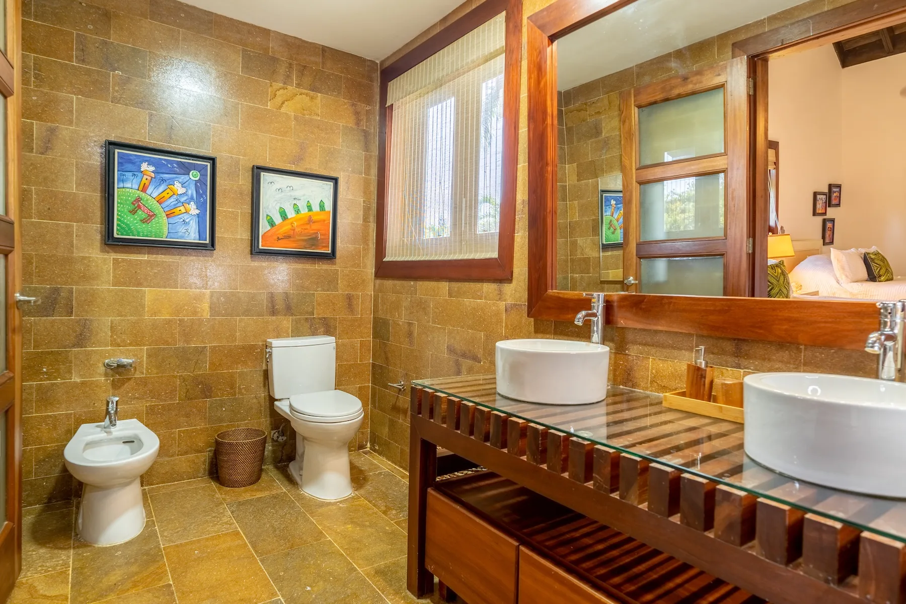 A bathroom with two sinks, a toilet, and framed artwork on the tiled walls.