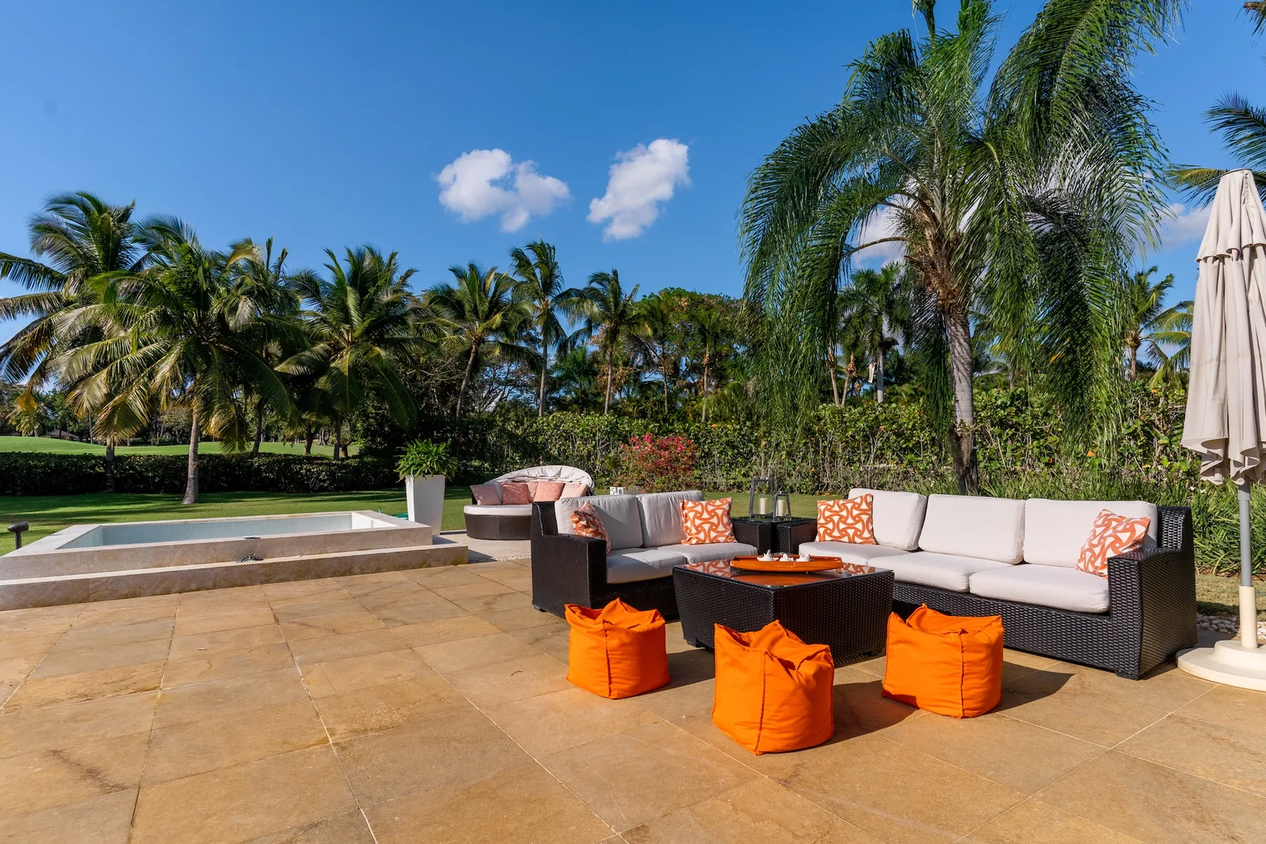 An outdoor patio seating area with cushioned furniture and bright orange poufs.
