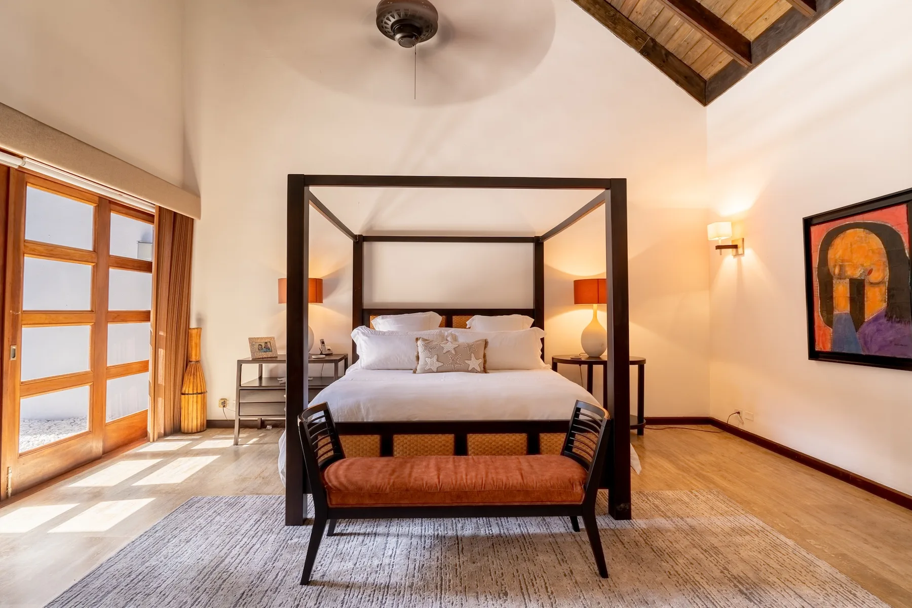 A bedroom with a four-poster bed, wooden floors, and large glass doors.