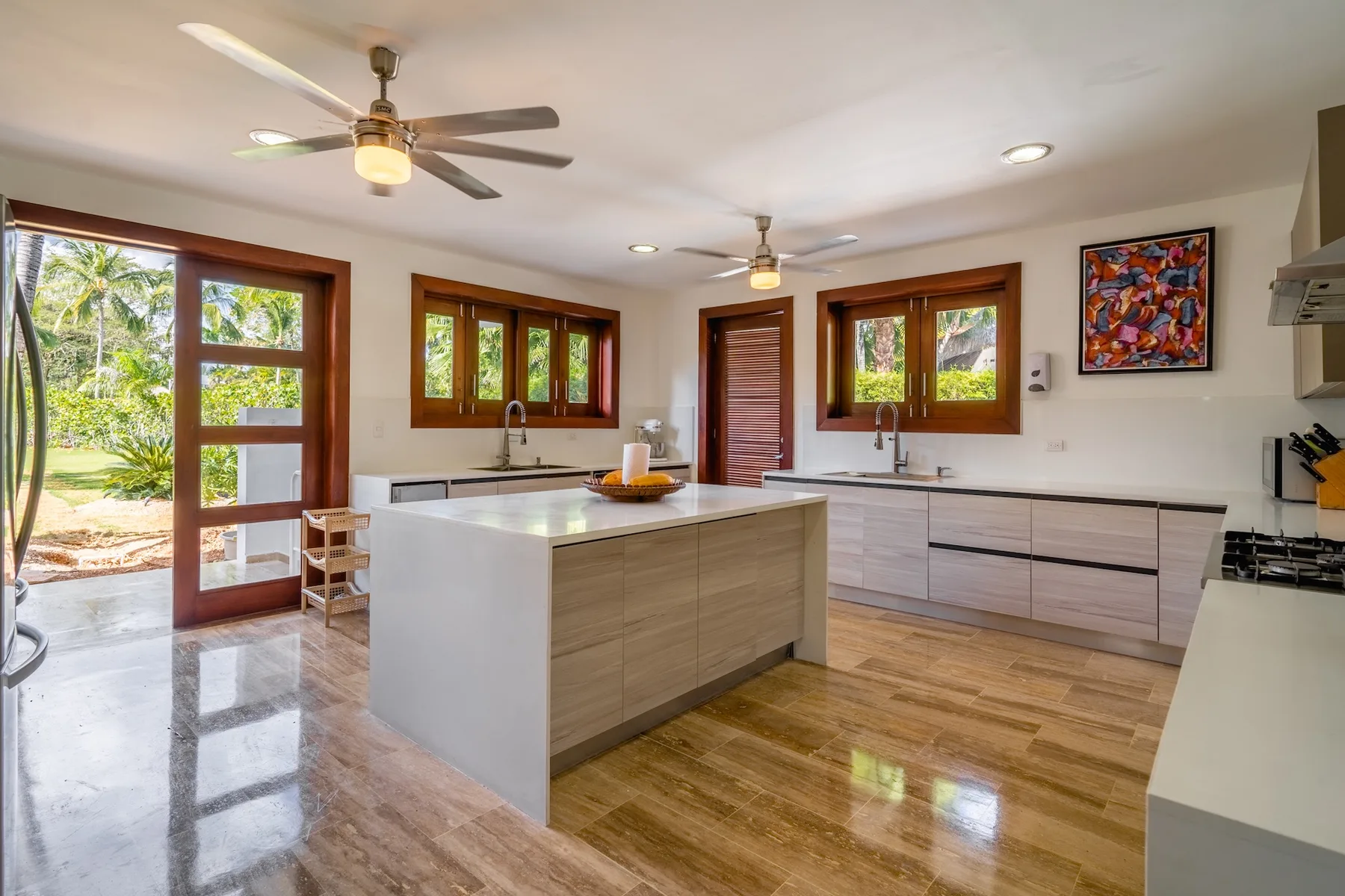 A bright kitchen with a large central island and windows overlooking greenery.