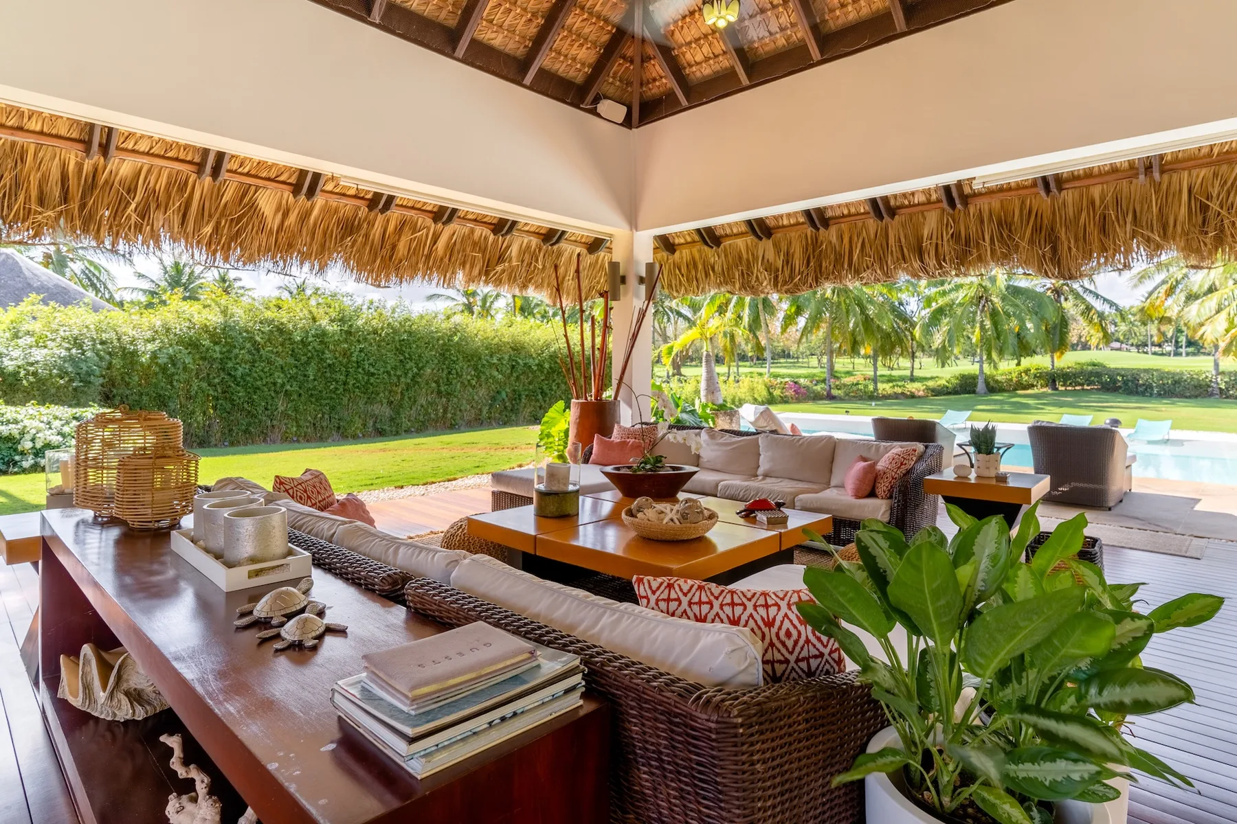 Open-air lounge with wicker seating and a thatched roof overlooking a garden.