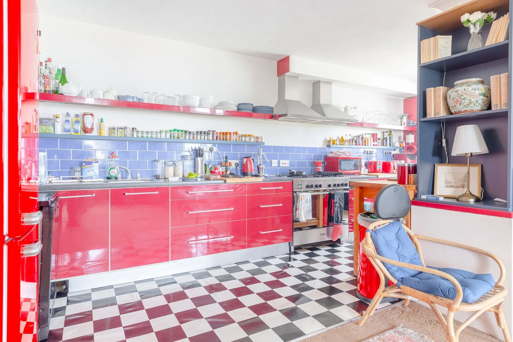 A bright kitchen with red cabinets, a tiled backsplash, and checkered flooring.