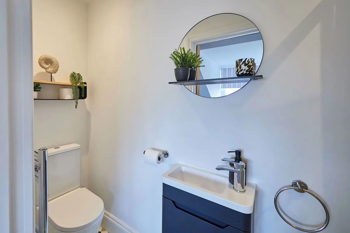 Un baño pequeño con lavabo, inodoro y espejo redondo en la pared.