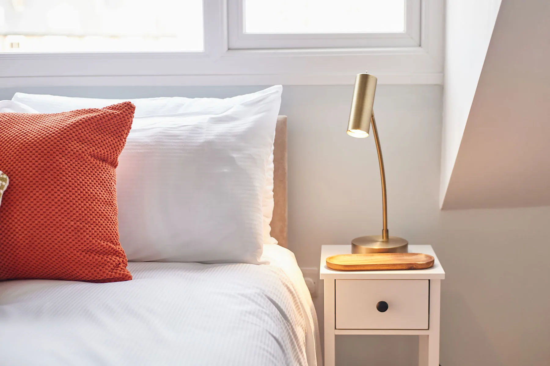 Dormitorio con una cama, un cojín rojo y una lámpara de noche.