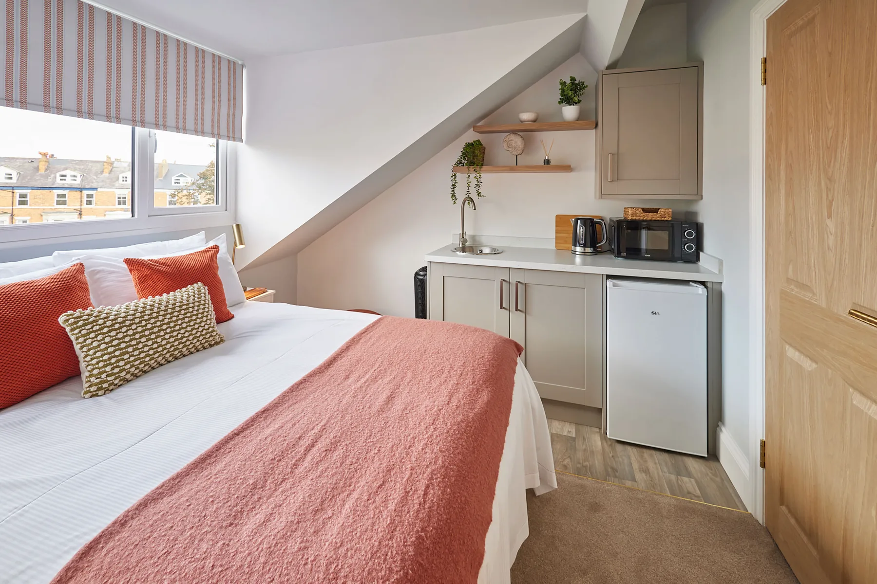 Dormitorio con una cama junto a una pequeña cocina y una ventana.