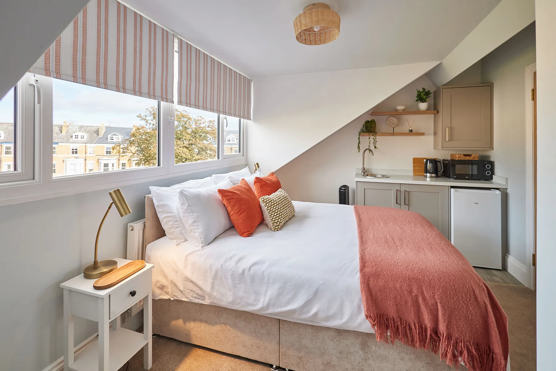 A bright bedroom with a bed beneath sloped ceilings and large windows.