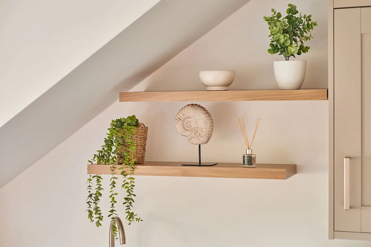 Una pared interior luminosa tiene dos estantes flotantes con plantas y objetos decorativos.