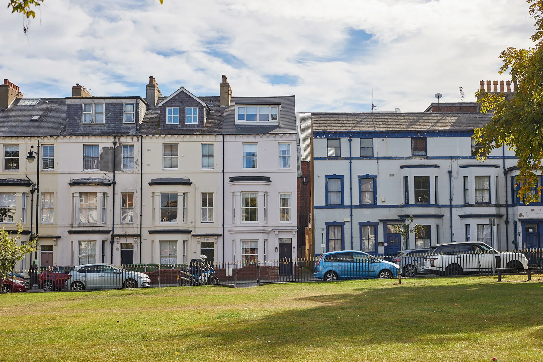 A row of attached townhouses faces a grassy lawn under a cloudy sky.