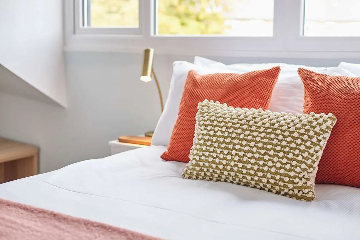 Un dormitorio con una cama blanca y cojines estampados de colores.