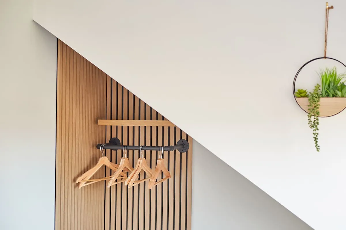 Un perchero de pared con perchas de madera está junto a una planta colgante.