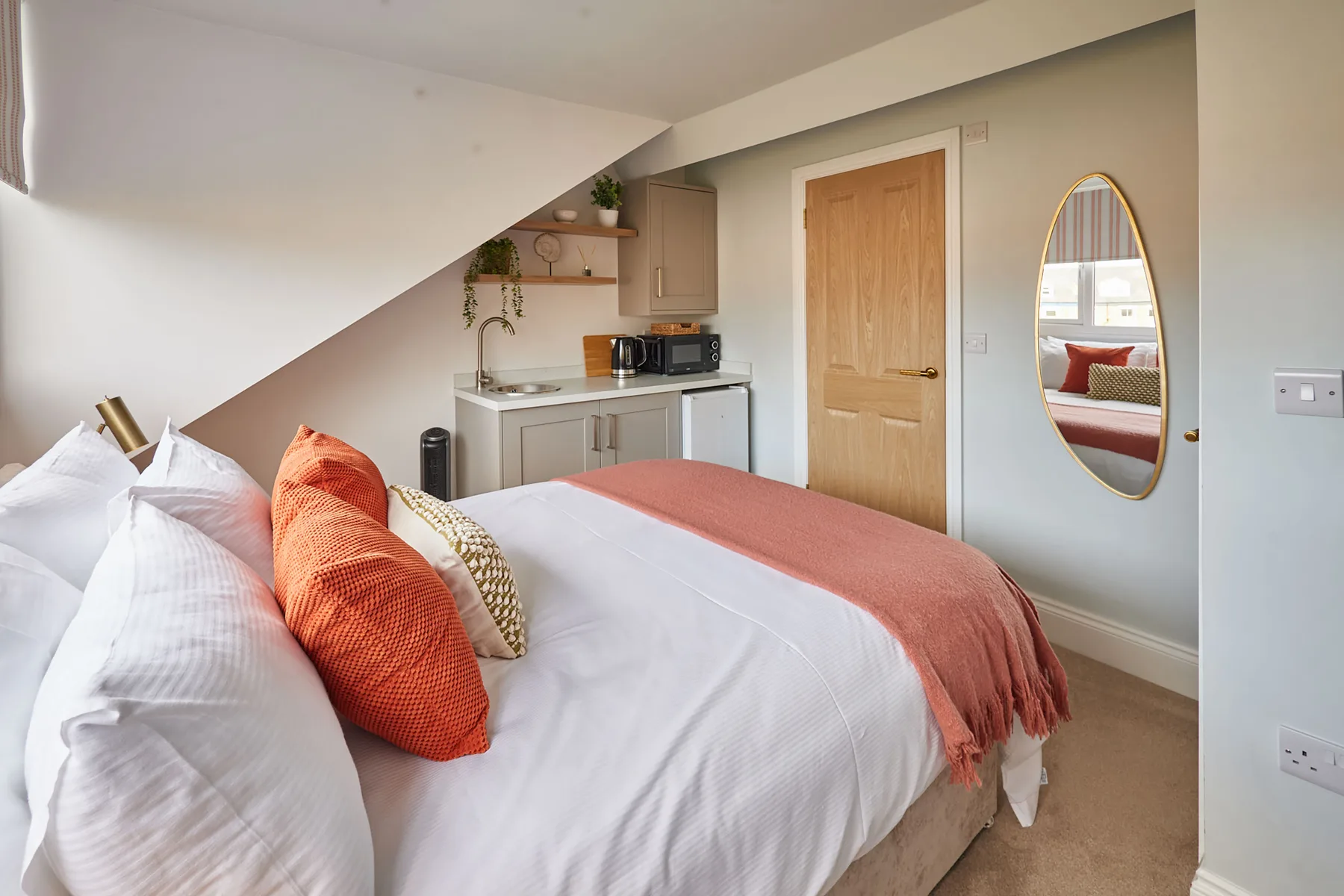Un dormitorio con una cama bien tendida y una pequeña cocina al fondo.