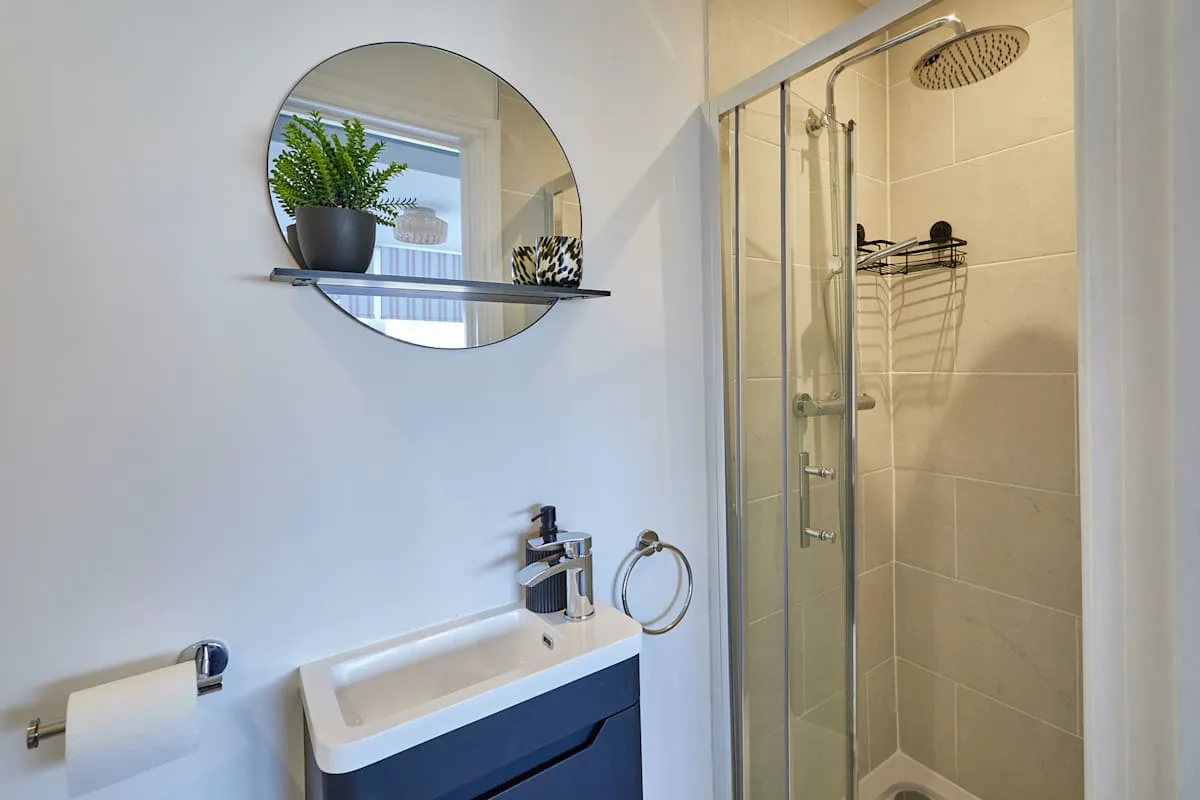 Un baño con lavabo, espejo redondo y ducha de vidrio.