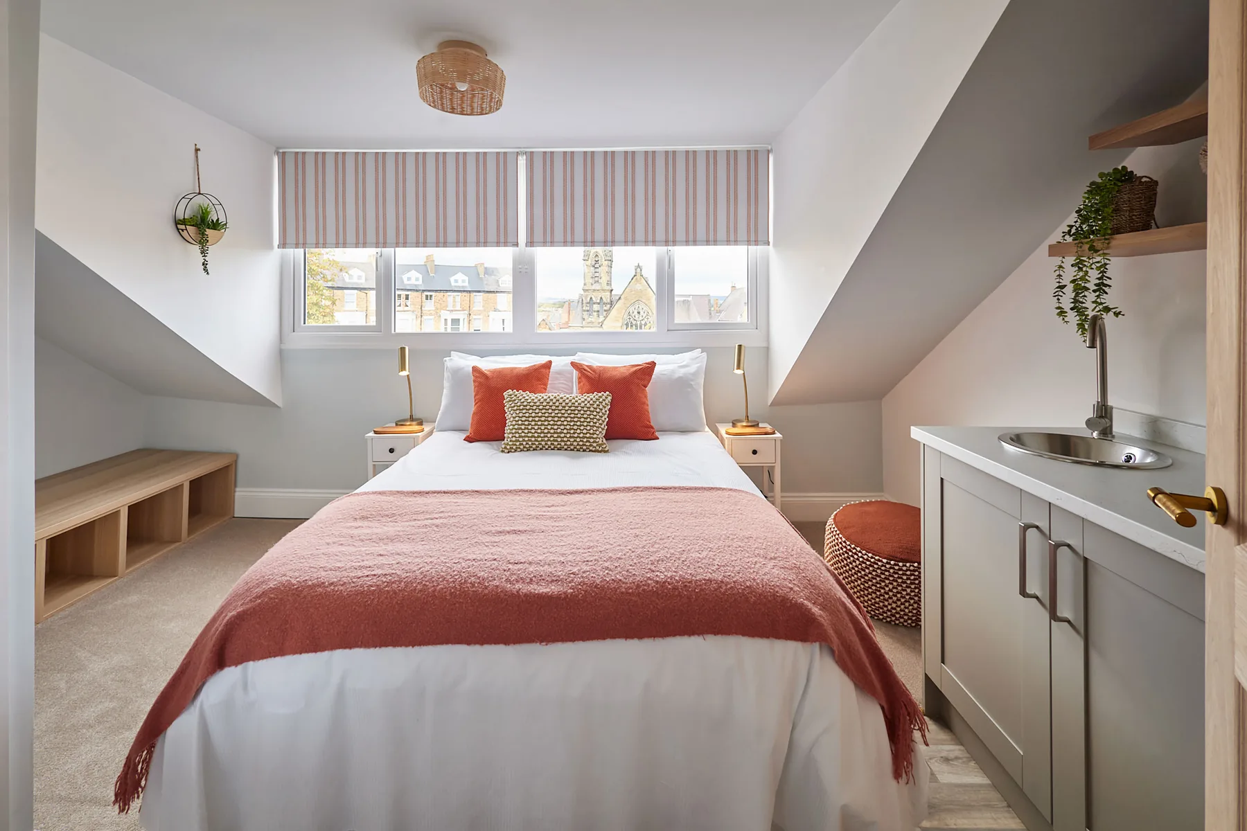 A bright bedroom with a bed beneath a wide window and a small sink vanity.
