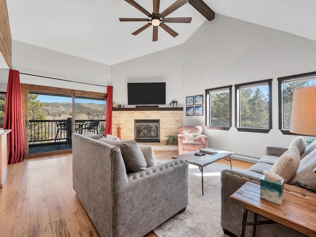 A bright living room with seating arranged around a fireplace and large windows.