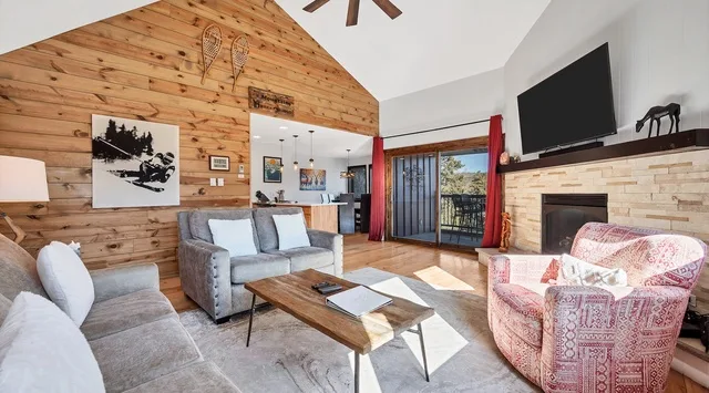 A bright living room with a wood-paneled wall and seating around a coffee table.