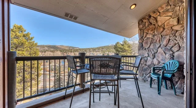 A covered balcony with outdoor seating overlooks a wooded landscape.