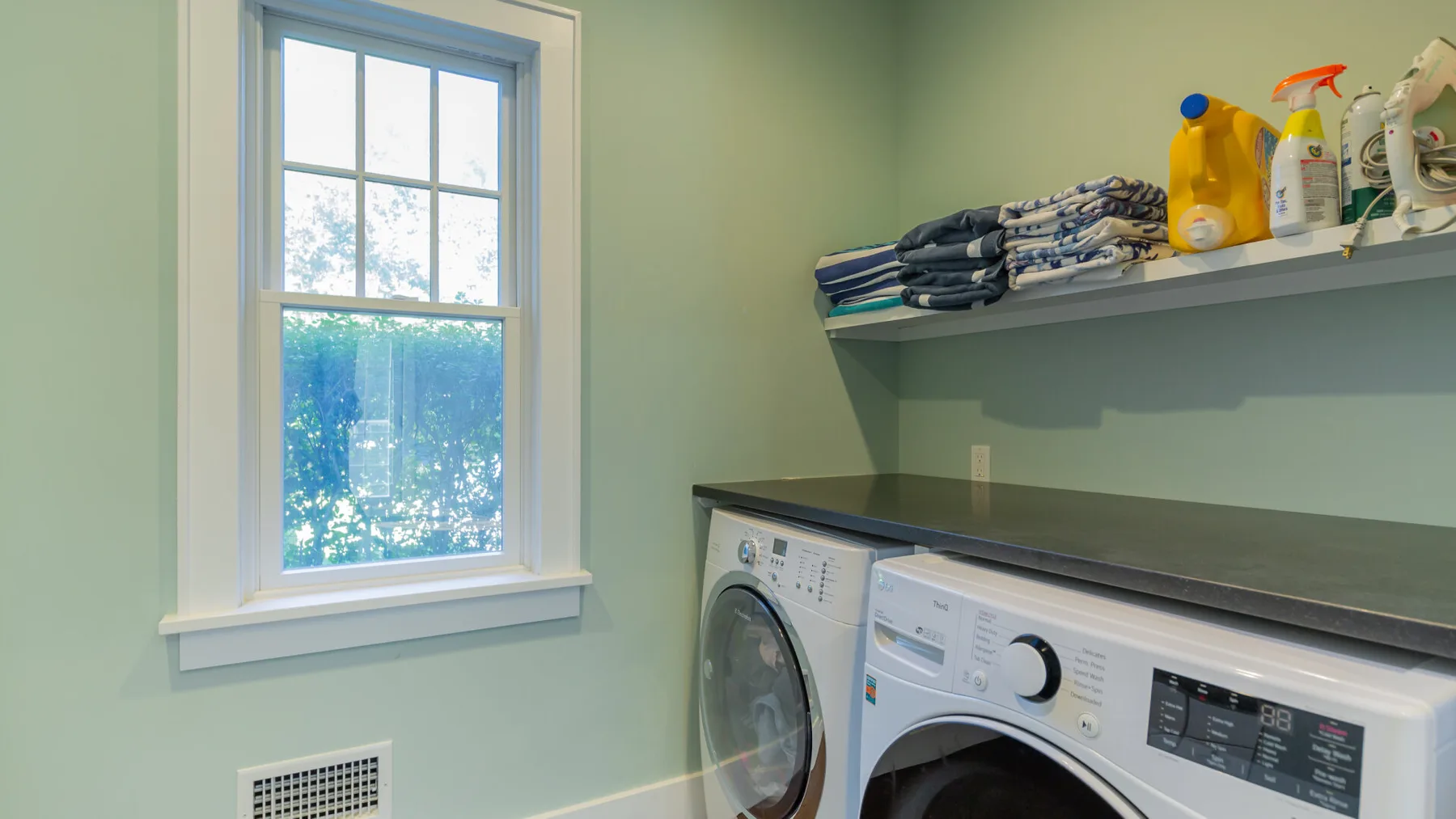 A laundry room with a washer and dryer beneath a shelf of folded linens.