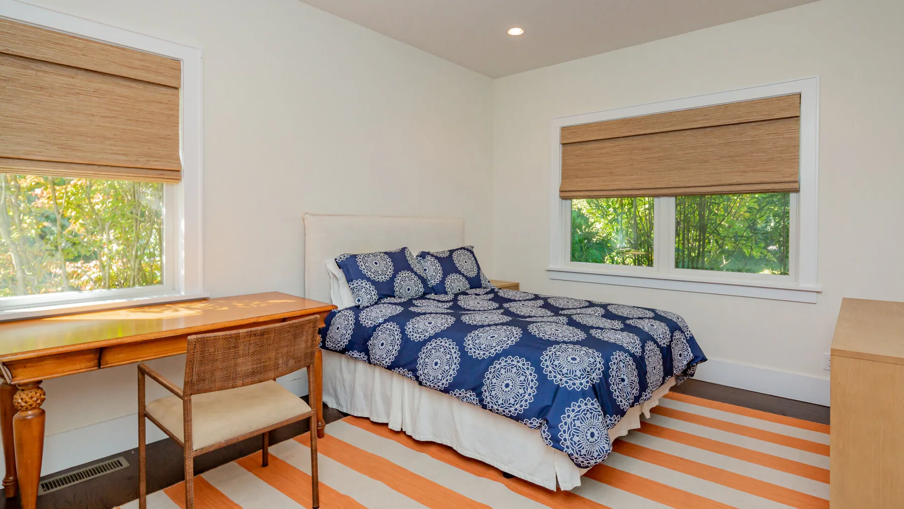 A bedroom with a bed dressed in blue patterned bedding and windows overlooking greenery.