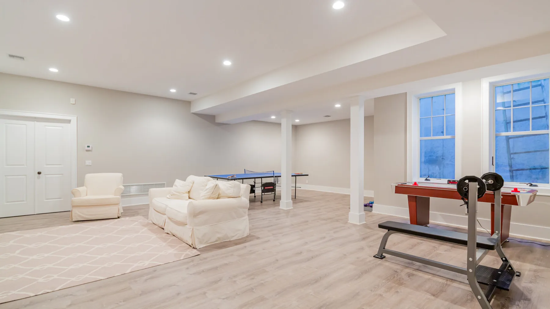A bright basement recreation room with seating and exercise equipment.