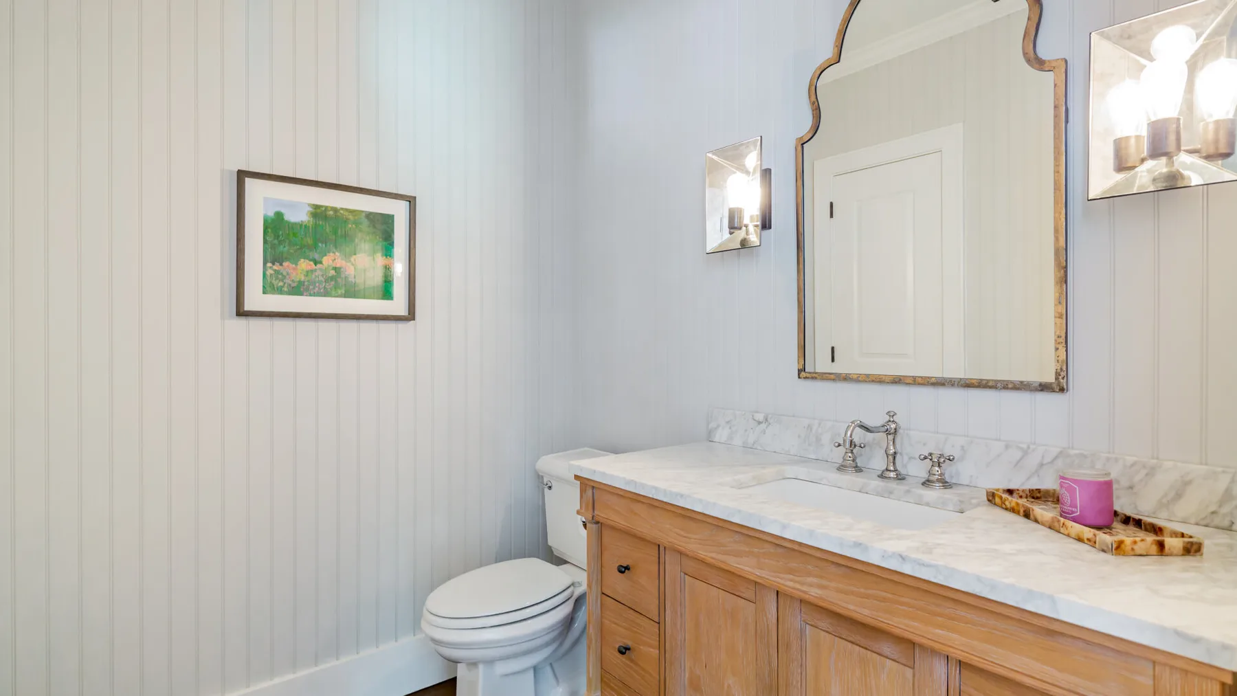 A bathroom vanity with a marble countertop, wall mirror, and toilet.