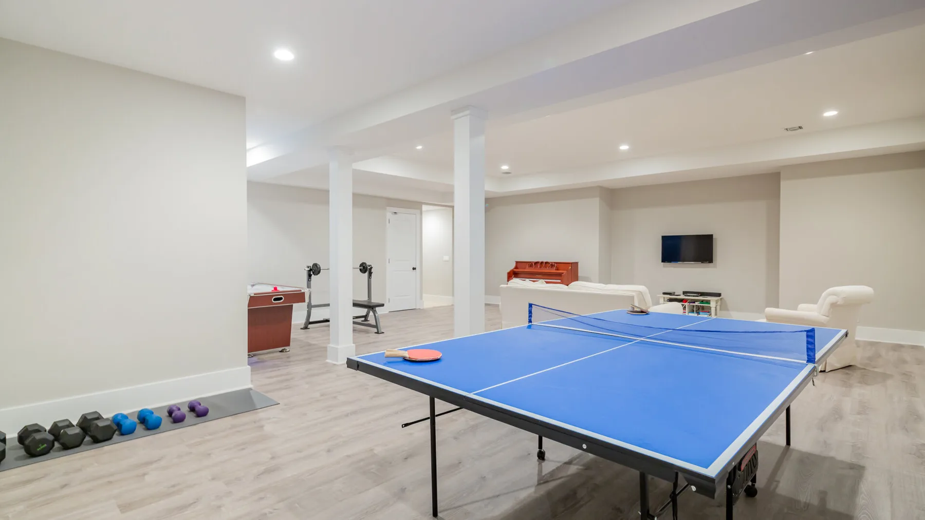 A spacious recreation room features a blue table tennis table and exercise weights.