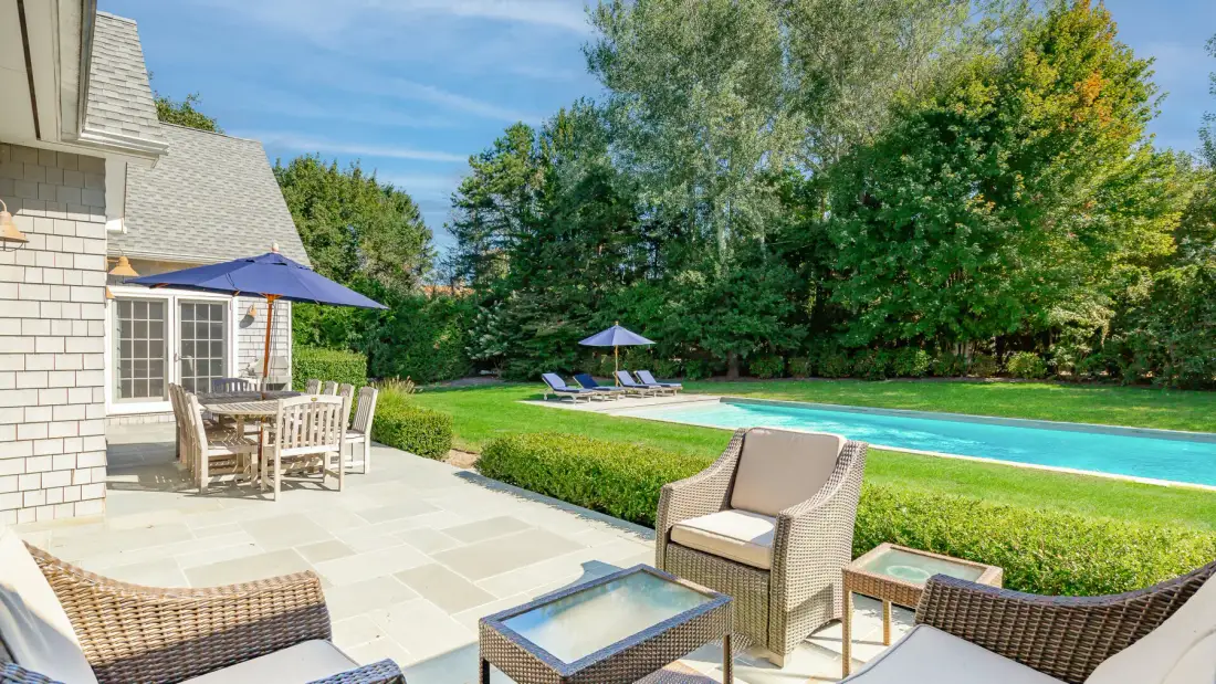A patio with outdoor seating overlooks a swimming pool and green lawn.