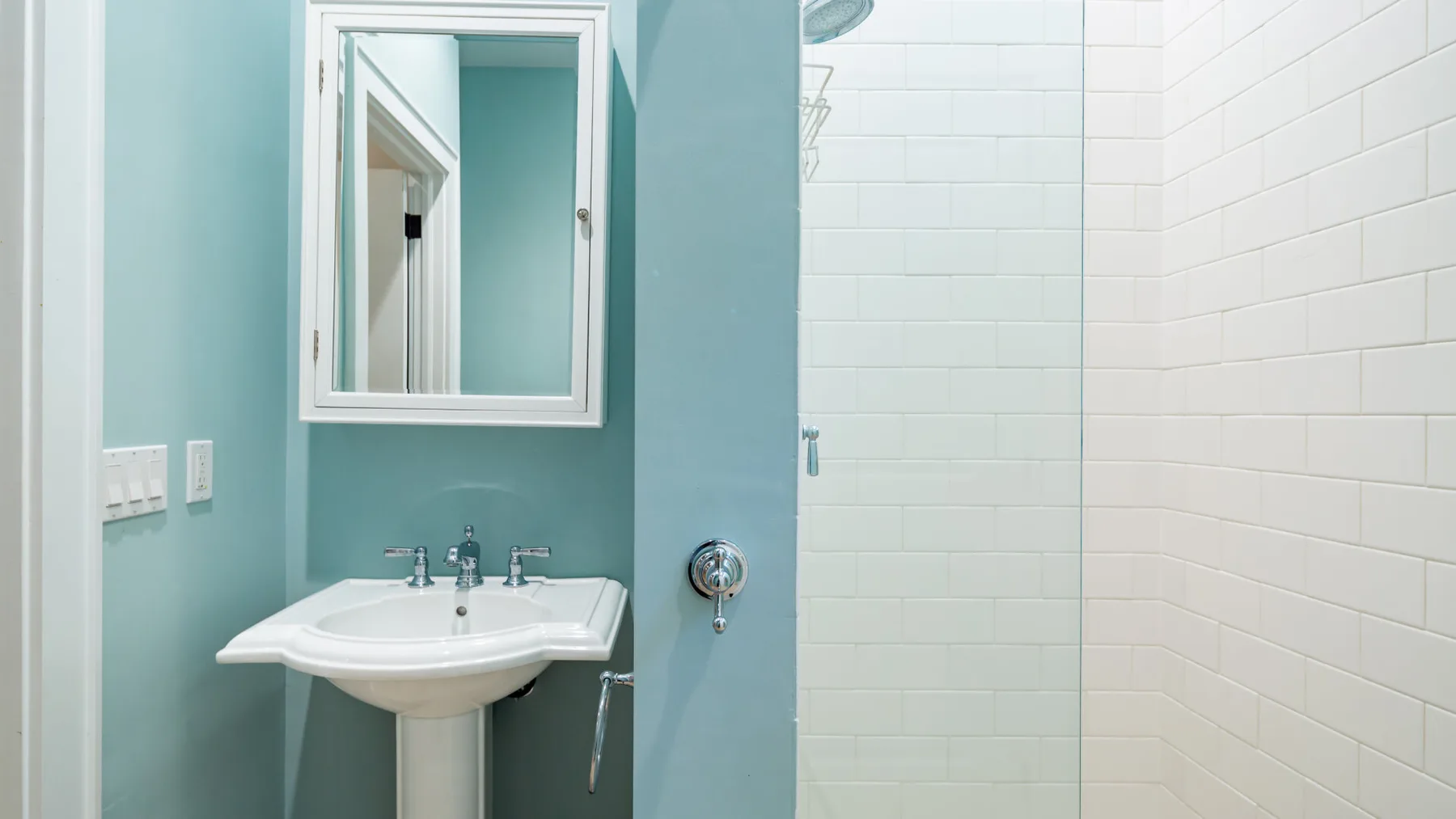 A bathroom with a pedestal sink, wall mirror, and tiled shower area.