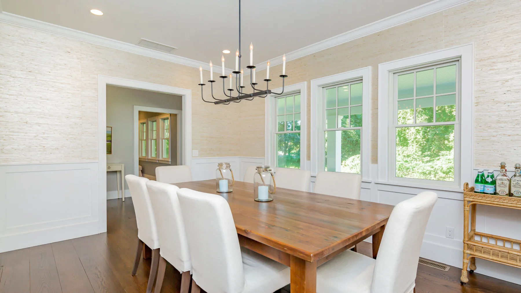 A bright dining room features a long wooden table and tall windows.