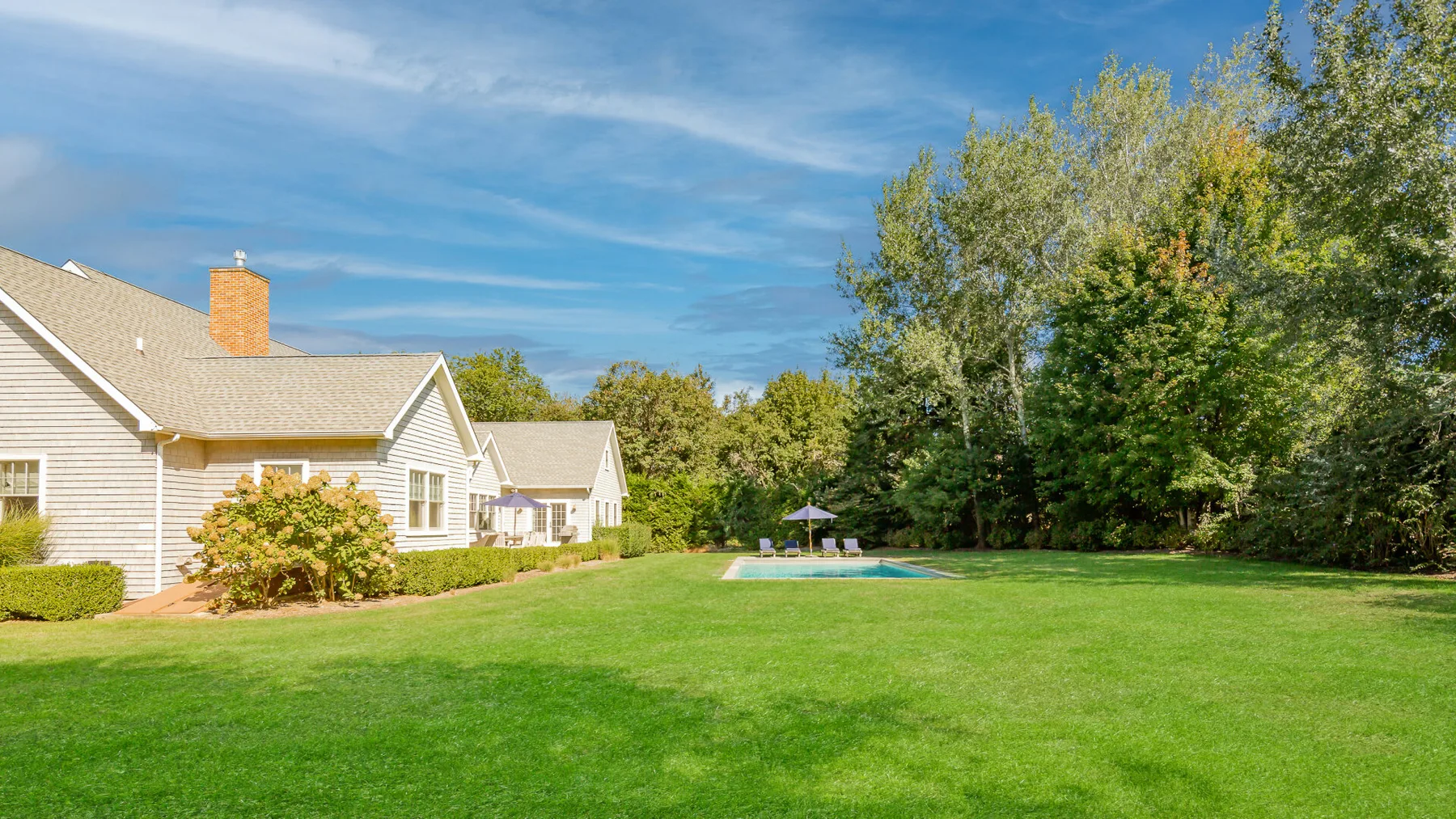 A large green lawn stretches between houses and a tree-lined edge.