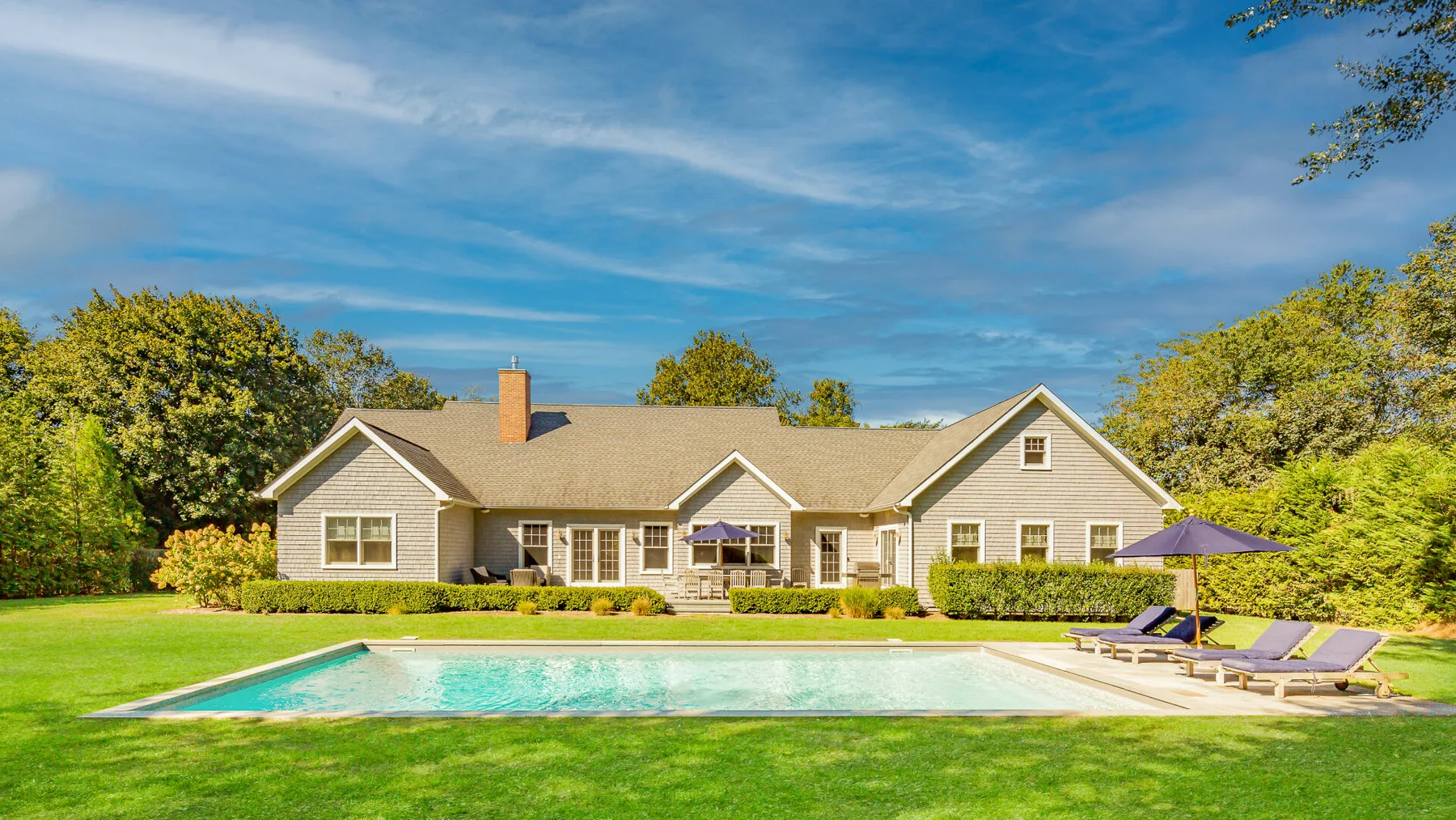 A large house stands behind a swimming pool and green lawn.