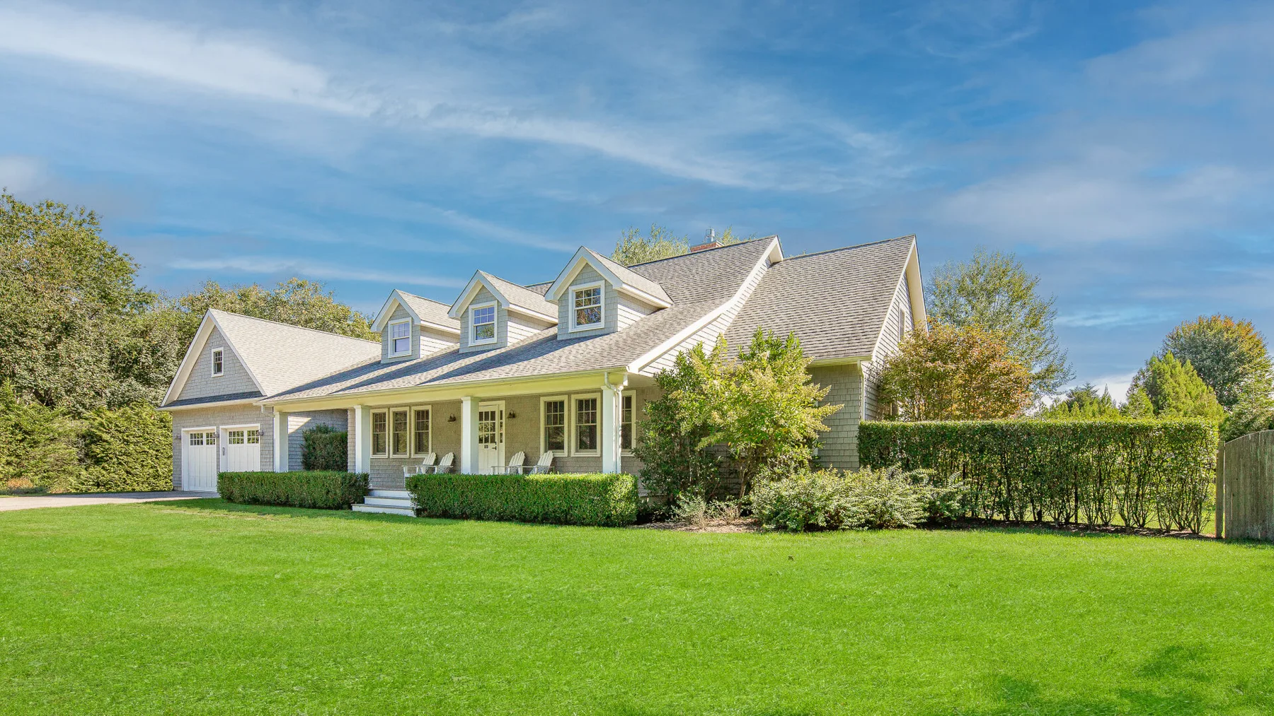 A large house stands beside a neatly trimmed lawn and hedges.