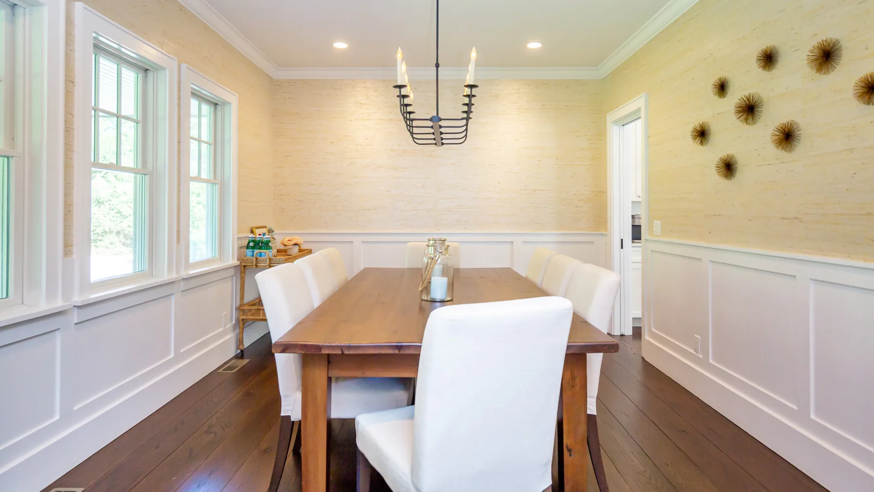 A dining room with a wooden table, white seating, and large windows.