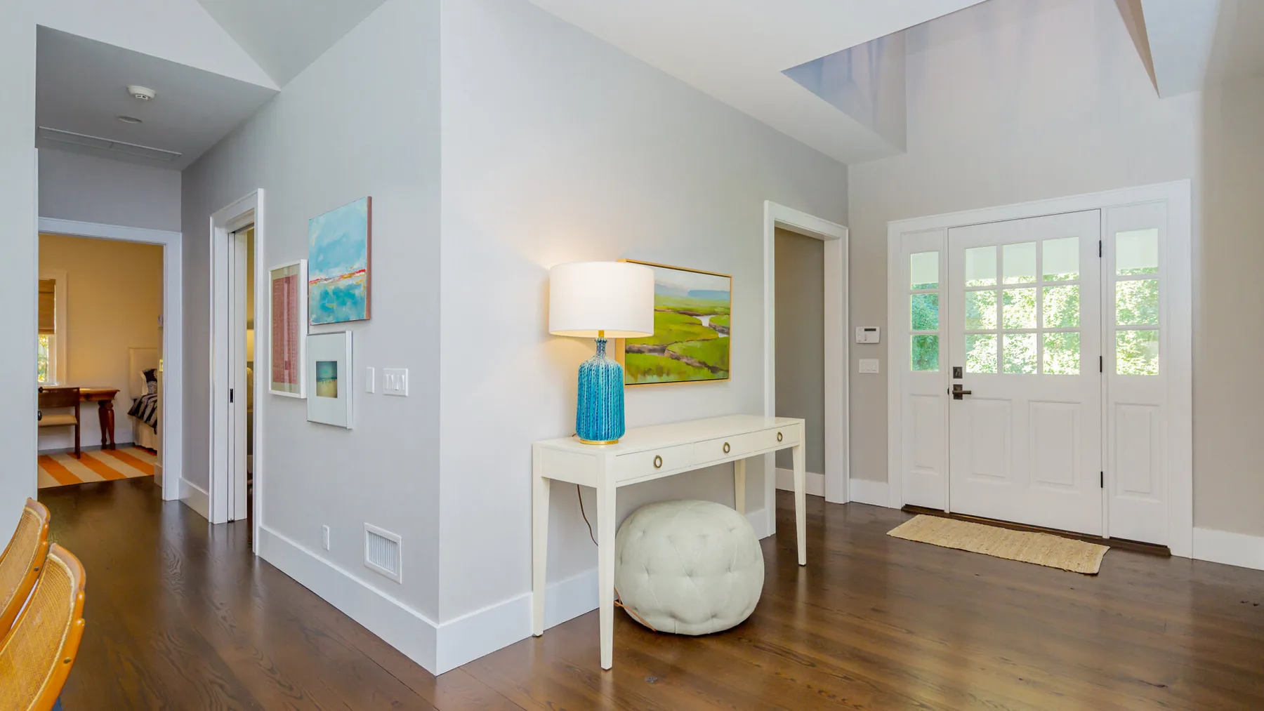 A bright entryway features a white front door, a console table, and wood flooring.