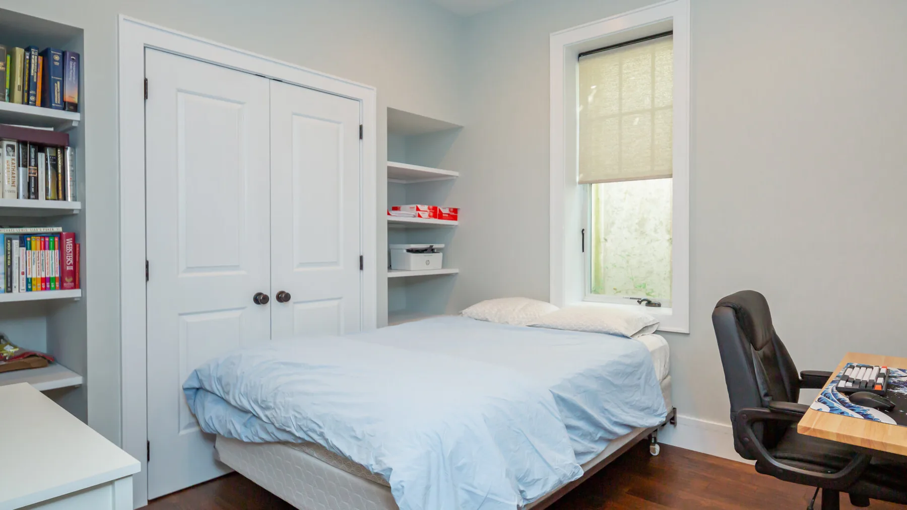 A bedroom with a bed, built-in shelves, and a window.