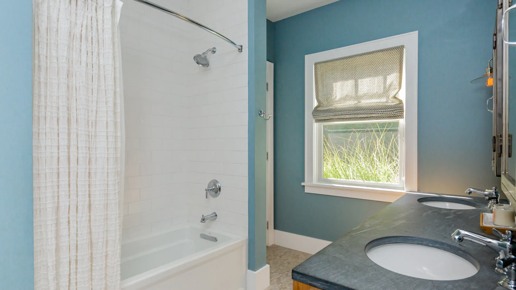 A bathroom with a bathtub, shower curtain, and vanity beside a window.
