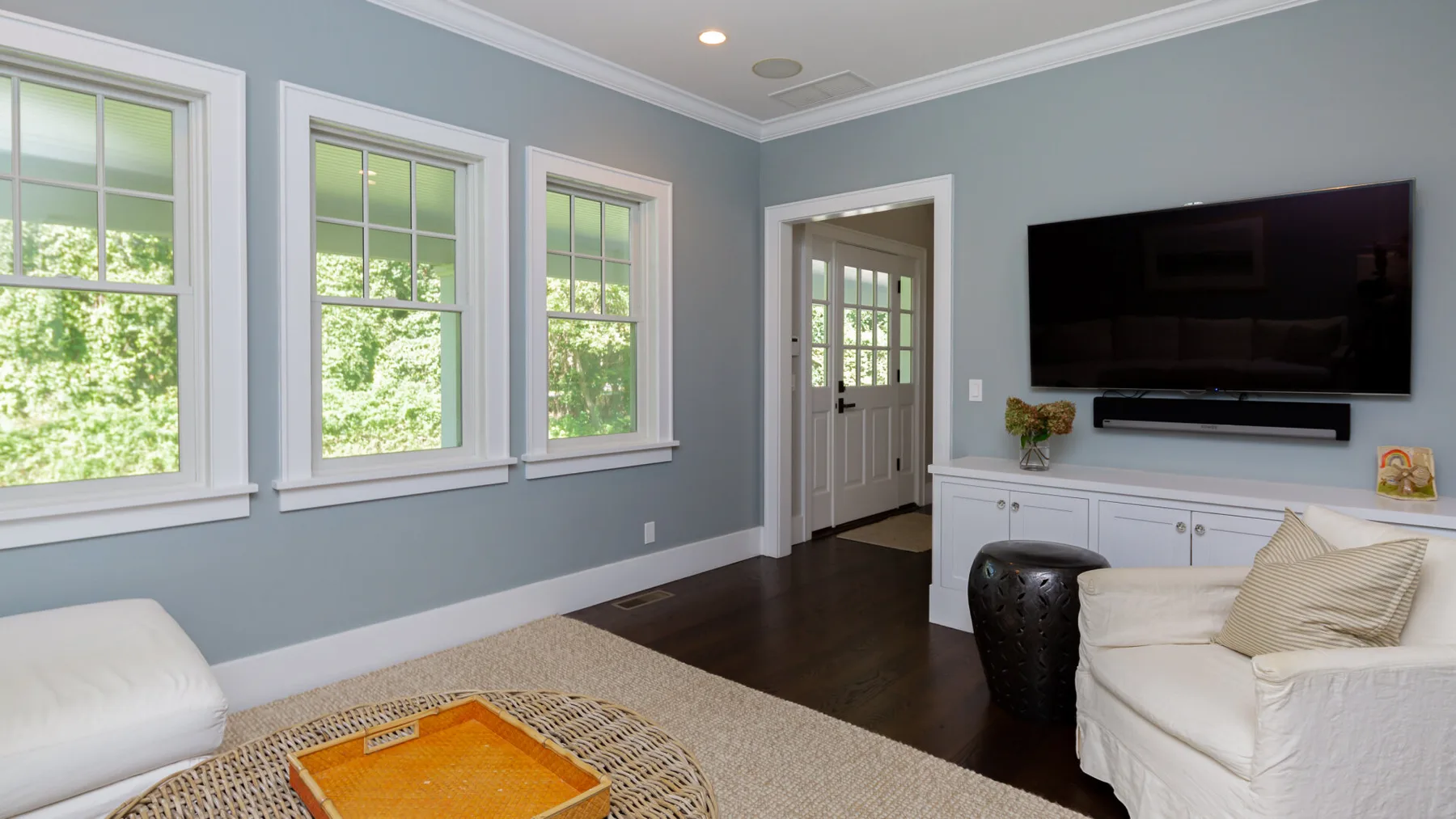 A bright living room with white seating, a television, and large windows.