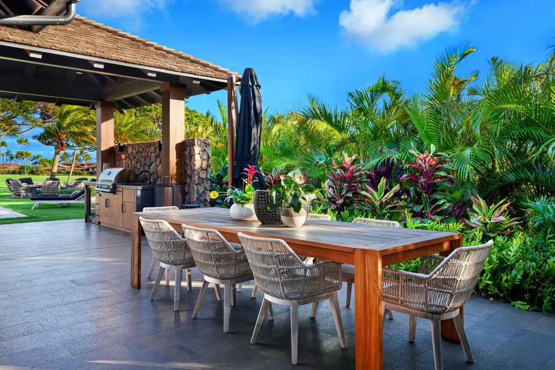 An outdoor dining area with a long table and tropical plants.