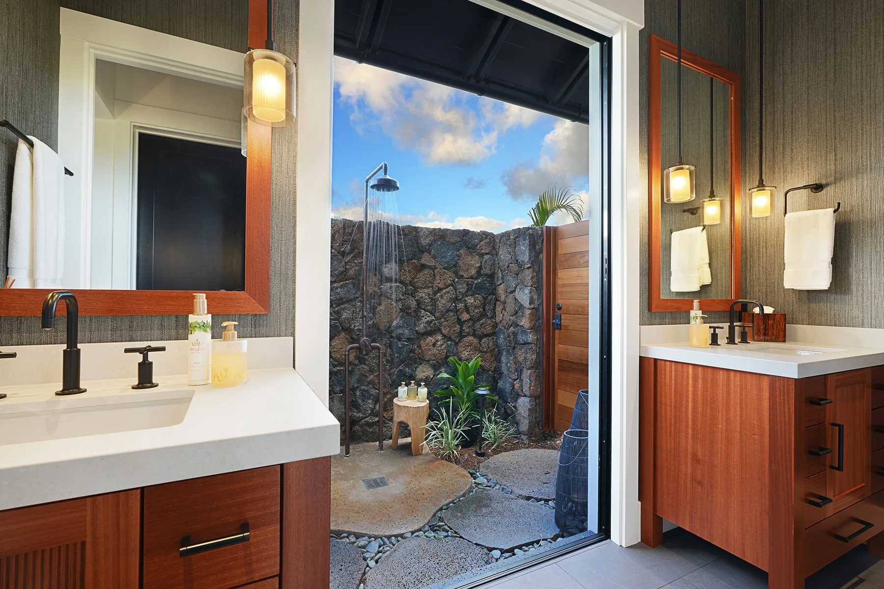 A bathroom vanity opens onto an outdoor shower area enclosed by a stone wall.
