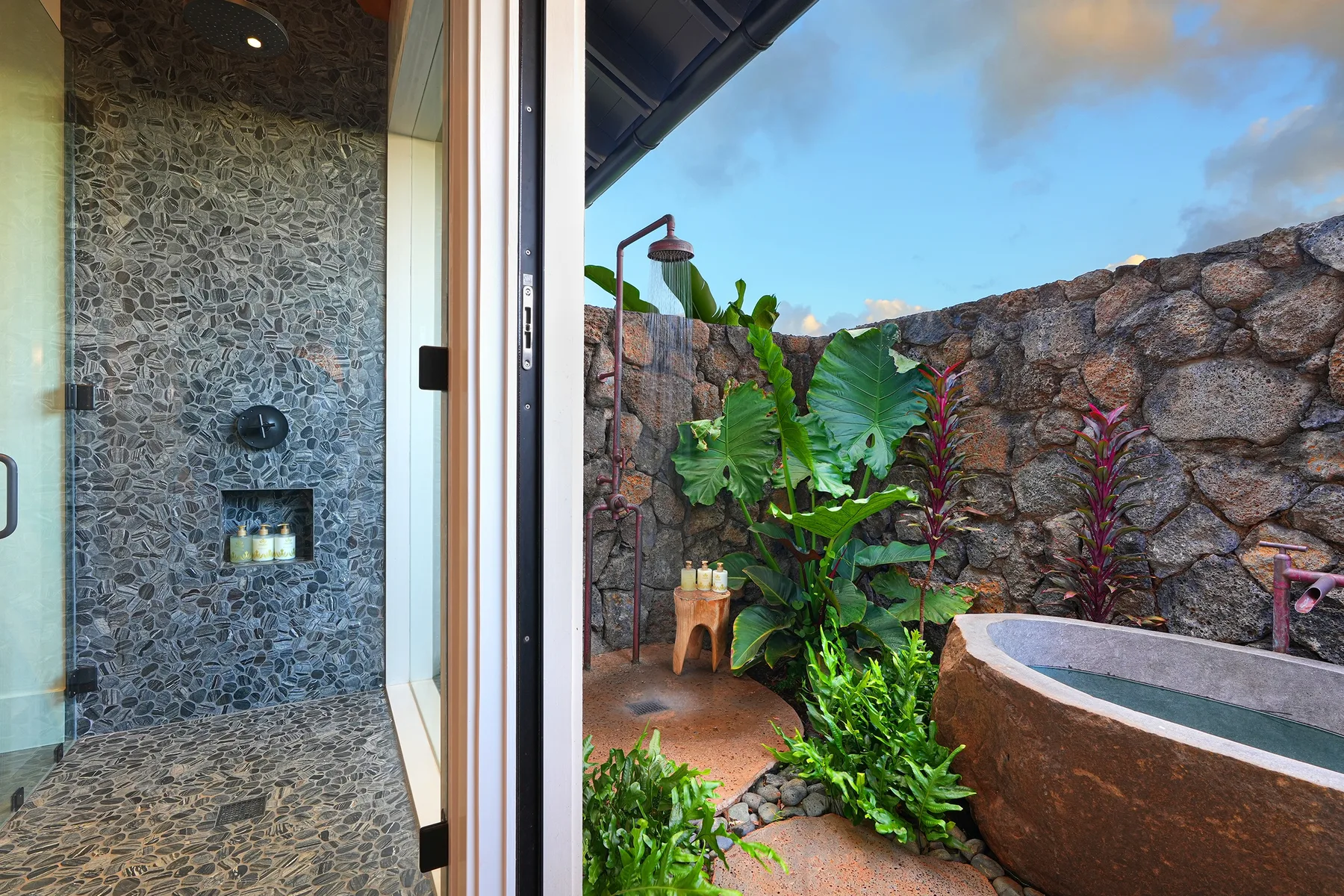 An outdoor stone-walled bathing area with tropical plants and a raised tub.